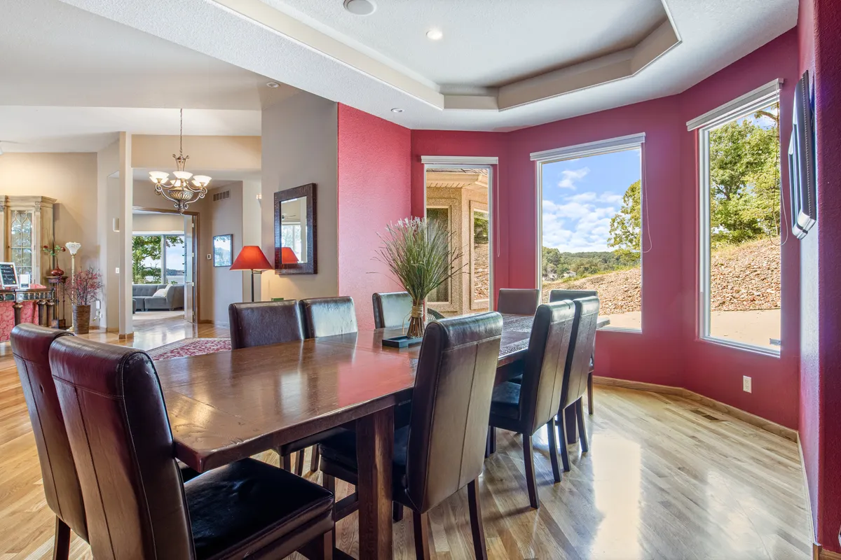A welcoming dining area with a large table set beneath a stylish chandelier, flanked by windows that bathe the space in natural light. Decorative touches like a vibrant plant and elegant table settings suggest the room is ready for lively family dinners, celebrations, or casual gatherings.