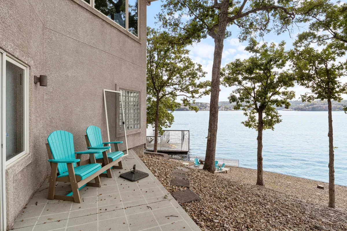 Turquoise Adirondack chairs are set along the lakeshore, framed by lush trees and overlooking a serene lake. The area exudes tranquility, offering ample space for relaxation and socializing, with a pristine water view and open skies ideal for pets to enjoy the outdoors beside their owners.