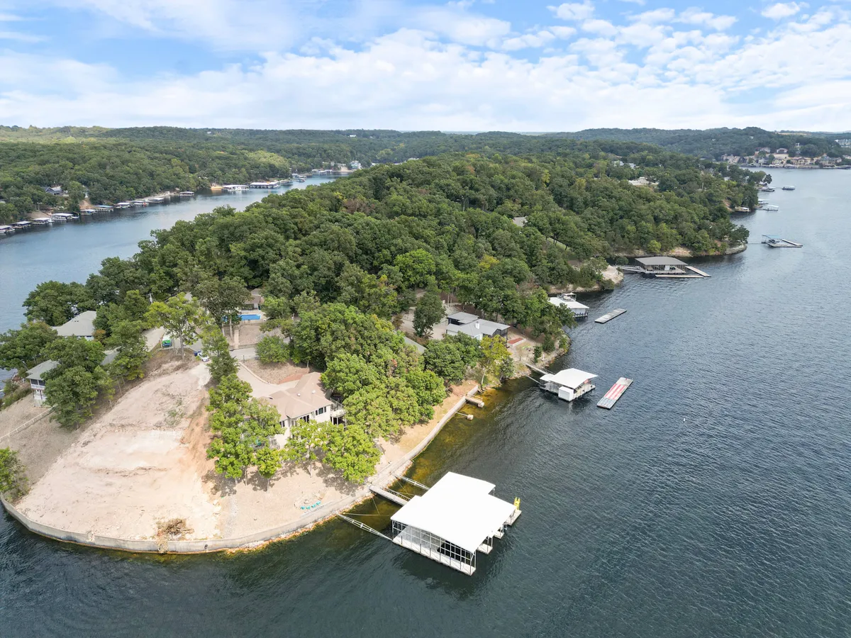 A wide view over the calm lake with a well-maintained dock featuring multiple boat slips, boats moored, and lush green trees surrounding the curving shoreline. The scene is tranquil, with hints of boating, fishing, swimming, and picnicking activities. The dock and water are bathed in soft natural light, suggesting either early morning or sunset hours.