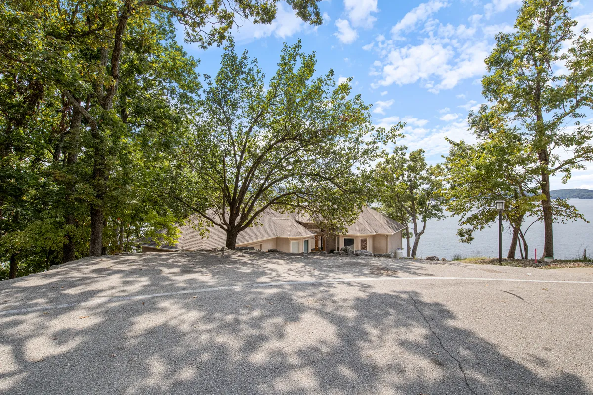 A large tree stands between the house and the lake, blending the comfort of home with the natural beauty of the outdoors. The scene invites picnicking, nature walks, and quiet mornings, with the lake offering a reflective, year-round backdrop.