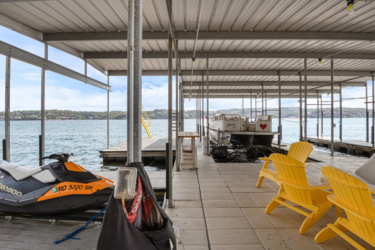 A vibrant lakeside scene featuring a jet ski docked by the water, several bright yellow Adirondack chairs arranged for relaxation, and a spacious docking area with clear access for boats and personal watercraft. The setting is lively and highlights both the adventure and tranquility of the private dock.