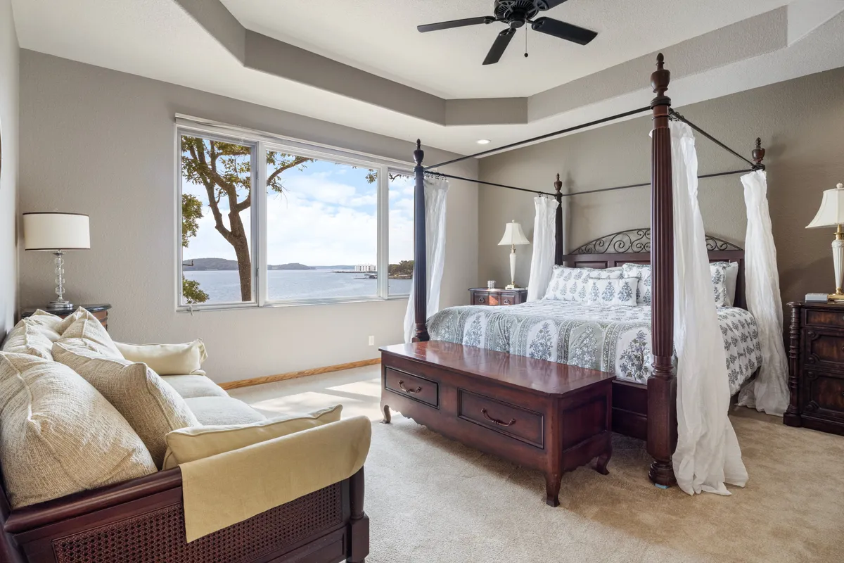 A calm and peaceful bedroom with a classic four-poster bed, large windows offering a scenic view, a cozy seating area, and wooden furniture. The atmosphere is intimate and restful, emphasizing comfort and classic elegance.