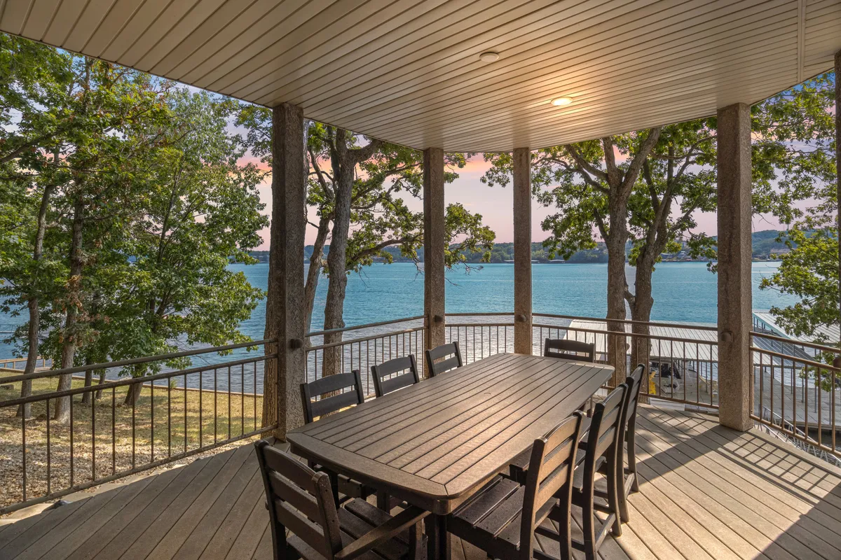 A cozy exterior deck with a dining table positioned to face the water, surrounded by trees. The scene evokes a sense of relaxed togetherness, with plenty of space for outdoor meals or games.