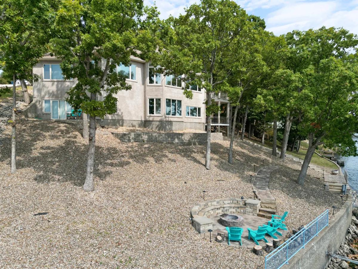 An inviting outdoor scene featuring a modern fire pit area with comfortable seating, perfectly positioned to take in the lakeside views. The house and trees frame the space, making it ideal for cozy evenings, stargazing, and gathering with friends and family under the open sky.
