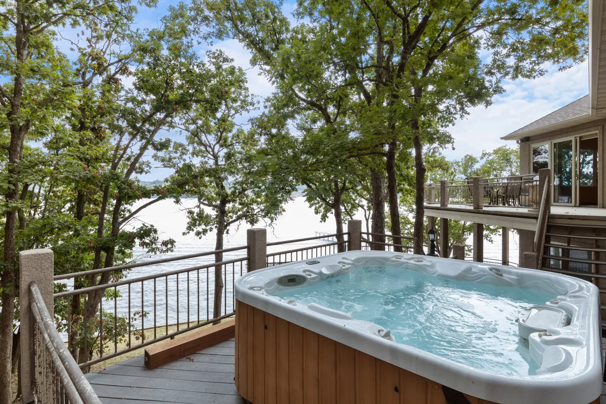 A serene exterior view of a spacious hot tub set on a deck, surrounded by lush trees and overlooking the tranquil lake. The area is perfect for unwinding after a day on the water, with plenty of space for friends and family to relax and enjoy the natural scenery.
