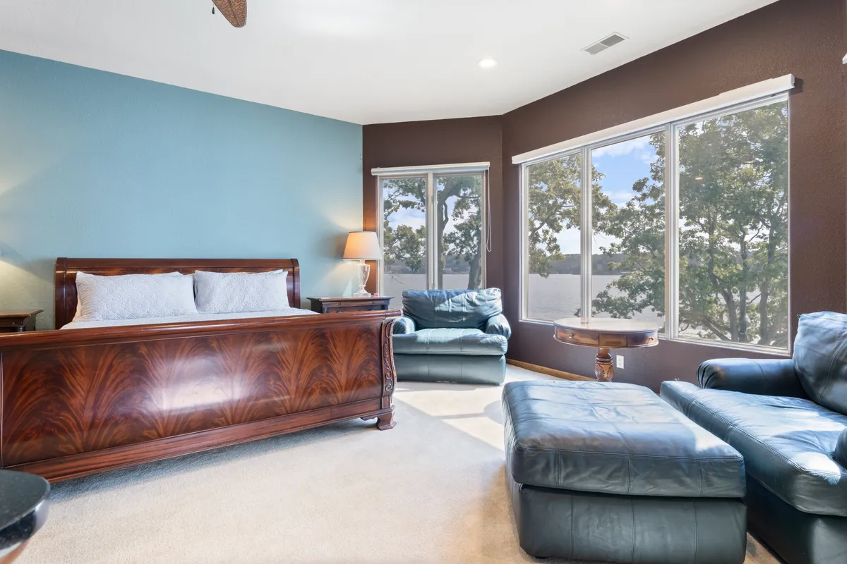 This image features a serene bedroom with a decorative headboard, large windows that allow natural light to flood in, and a cozy seating area. The room exudes tranquility and warmth, offering a peaceful space to unwind after a busy day.