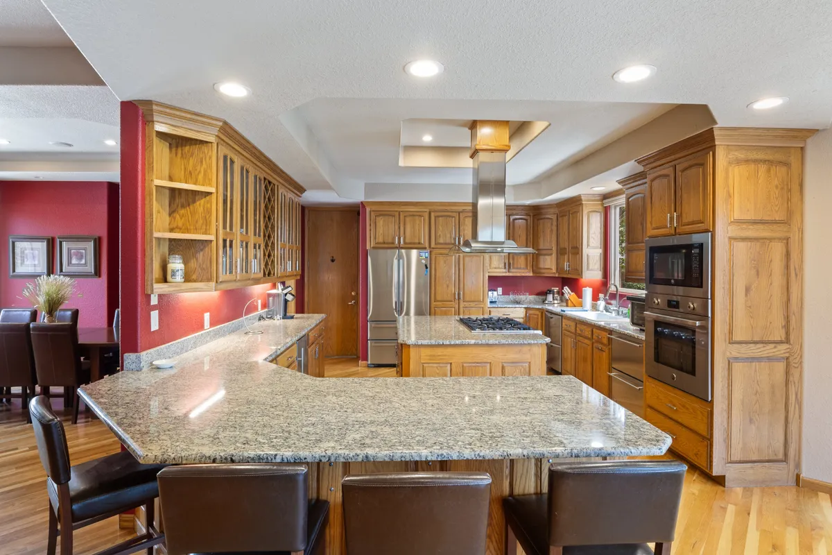 A modern, fully stocked kitchen featuring granite countertops, wood cabinetry, stainless steel appliances, and a spacious kitchen island. The layout encourages group meal prep, cooking together, and entertaining guests, emphasizing both function and warmth.